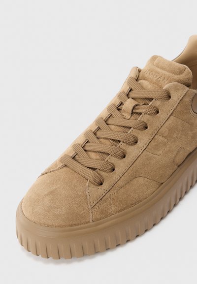 Light brown suede sneaker with thick rubber sole, matching laces, and detailed stitching on a white background.