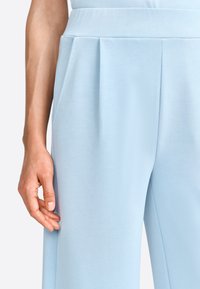 Pantaloni a gamba larga azzurro chiaro con una texture liscia, caratterizzati da una vita piatta e tasche laterali. Dettaglio delle pieghe per una struttura migliorata.
