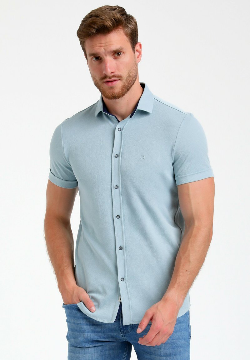 Polo shirt a maniche corte di colore azzurro chiaro con un tessuto testurizzato, dotato di una chiusura a bottoni frontale e un piccolo logo sul petto.