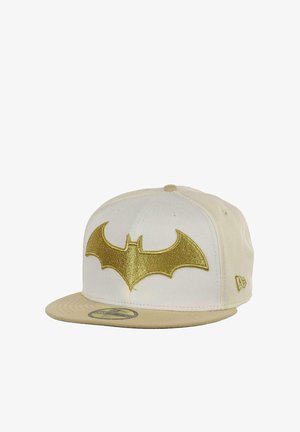 Cream snapback cap featuring a golden Batman logo on the front. The bill is a darker cream, with stitching accents and a flat visor design.