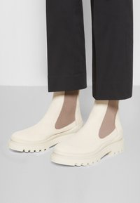 Skórzane botki Chelsea w odcieniu off-white z żeberkowym brązowym elastycznym wykończeniem, masywnymi beżowymi podeszwami i gładkim, minimalistycznym wzorem.