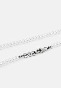 Perlenekke med uniforme, runde, hvite perler, sølvklips med "ICON" gravering, jevn tekstur og klassisk design.