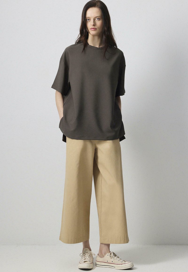Overdimensioneret brun bomulds t-shirt og beige brede bukser, suppleret af lyse sneakers. Simpelt design, glat tekstur.