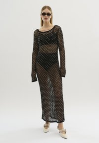 Rochie din plasă neagră cu decorațiuni rotunde din argint, mâneci lungi și decolteu rotund. Pur poate fi purtată peste un bikini negru; asociată cu încălțăminte cu vârf ascuțit.