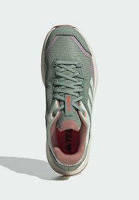 Baskets de sport vert clair avec une tige en maille texturée, des accents roses et une semelle blanche. Présente des lacets gris et un logo sur la languette.