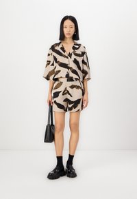 Beige cropped paita ja matching lyhyet housut, joissa on musta ja ruskea abstrakti kuvio. Musta laukku, nilkkaan yltävät sukat ja jykevät mustat kengät viimeistelevät ilmeen.