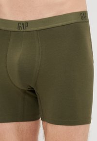 Boxeri din bumbac de culoare verde măsliniu, cu un logo negru țesut „GAP” pe banda elastică și cusături flatlock pentru confort.