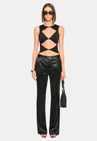 Black cut-out top with silver hardware details, paired with high-waisted black satin trousers. Model holds a textured black handbag.