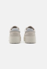 Beige Wildlederschuhe mit einem glatten grauen Lederakzent an der Ferse, ausgestattet mit einer dicken off-white Sohle und geprägter Markierung an der Ferse.