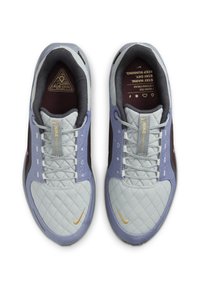 Baskets gris clair avec une texture matelassée, des accents violets et des détails dorés sur la languette et le côté, avec un design à lacets.