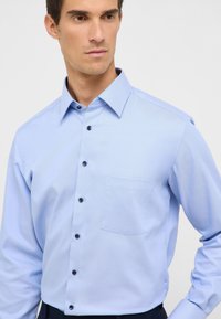 Camicia a maniche lunghe blu chiaro con tessuto testurizzato, taschino sul petto e bottoni scuri. Include un collo classico e una vestibilità su misura.