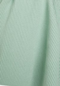 Miętowo-zielona teksturowana tkanina z prążkowanym wzorem oraz subtelnymi różnicami w splocie, tworząca miękki i lekki wygląd.