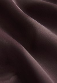 Tessuto borgogna profondo con una texture liscia e morbida, caratterizzato da sottili motivi a onda e una leggerissima lucentezza, creando una ricca profondità visiva.