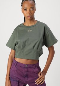 Olivengroene cropped t-shirt met korte mouwen, voorzien van een subtiel logo in het midden en een zachte textuur. Draag het met paarse broeken.