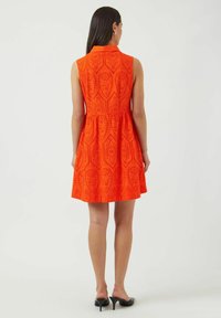 Oranssimekko ilman hihoja, jossa on kaulus, teksturoitu kuviokangas, jossa on leikkuurei'ityksiä, vyötärö kiristetty ja helma liehuva, yhdistettynä mustiin korkokenkiin.