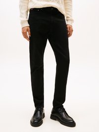 Jeans negros de mezclilla, con corte recto, cierre de botón y bolsillos clásicos. Combinados con zapatos negros con cordones y un suéter crema.