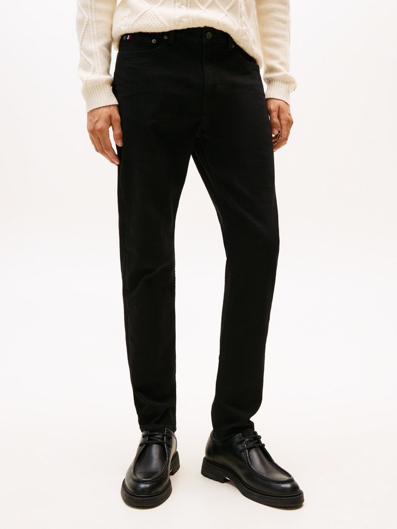 Jeans negros de mezclilla, con corte recto, cierre de botón y bolsillos clásicos. Combinados con zapatos negros con cordones y un suéter crema.