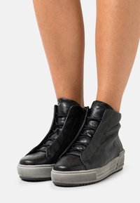 Czarne sneakersy za kostkę z teksturowanym wykończeniem, wyposażone w zamknięcie na zamek z przodu, detale z sznurowaniem oraz szarą gumową podeszwę.