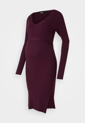 Zwangere jurk in donkerpaars, gemaakt van ribbelbrei. Heeft lange mouwen, een diepe V-hals, een ceintuur op de taille en zijsplitten voor extra comfort.