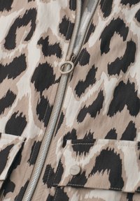 Beige og sort leopardprintstof med en sølv lynlås og klaplomme med en beige trykknap.