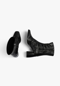 Botines de cuero negro con diseño fruncido, punta cuadrada y tacón grueso; cremalleras laterales que añaden un detalle funcional.