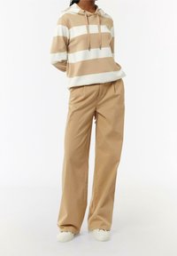 Sudadera con capucha a rayas beige y blanca con cordón, combinada con pantalones beige claros de pierna ancha y zapatillas blancas. Tejido suave y ajuste relajado.