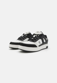 Fekete-fehér sneaker, texturált felső résszel, éles kontrasztos varrással, párnázott nyakkal és logóval a nyelvén. Gumitalp.