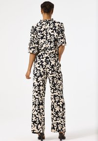 Zweiteiliges Outfit mit einem schwarzen und creamfarbenen Blumenmuster. Das Oberteil hat kurze Puffärmel und einen rüschigen Ausschnitt; die Hose hat weite Beine.