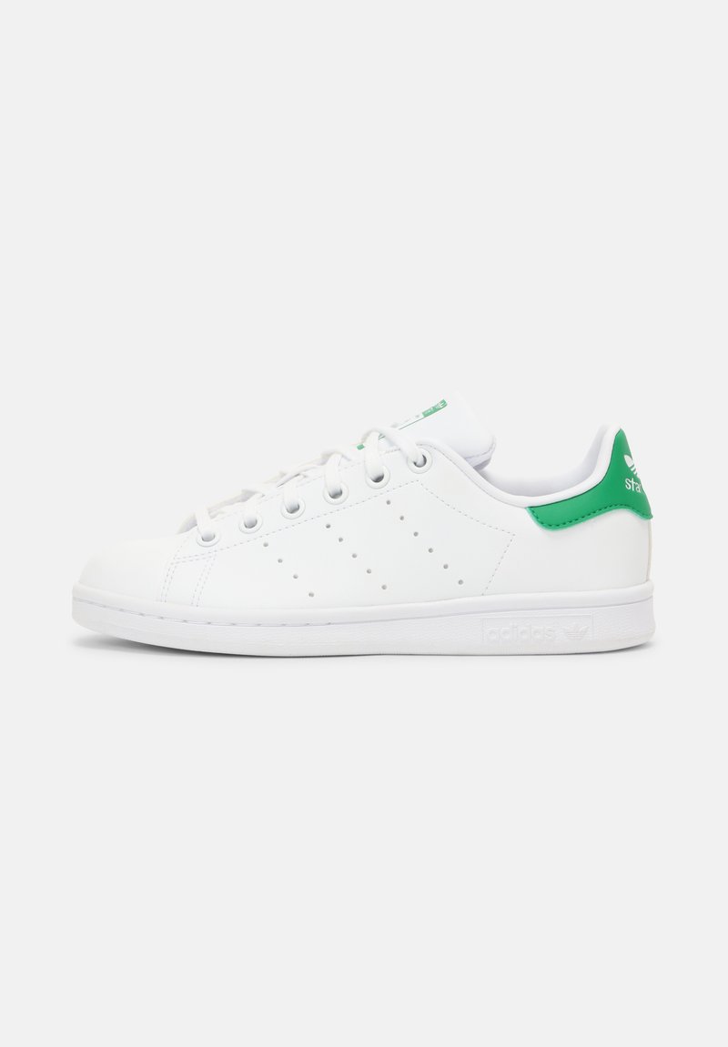 Zapatilla de cuero blanca con detalles en verde en el talón y la lengüeta, con perforaciones en los laterales, seis ojales y una suela de goma.