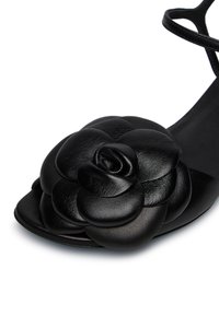 Sandal in pelle nera con un design floreale sulla punta. Presenta un motivo di fiori stratificati e testurizzati e una sottile cinghia alla caviglia.