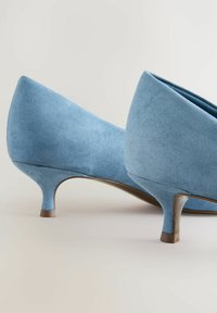 Zapatos de tacón alto de ante azul con punta afilada y diseño acampanado. Los tacones miden aproximadamente 5 centímetros de alto y tienen un acabado suave.