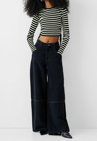 Pantalones negros de pierna ancha con costuras en contraste, combinados con una blusa de manga larga a rayas en blanco y negro.