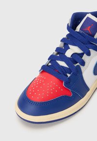 Baskets en cuir bleu et rouge avec un bout perforé rouge, une section médiane blanche et des accents bleus. Elles disposent de lacets bleus et d'un logo sur la languette.