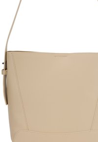 Beige leren schoudertas met een slanke schouderband en een minimalistisch ontwerp, voorzien van nette stiksels langs de randen.