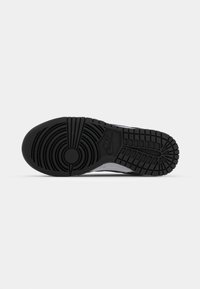 Semelle en caoutchouc noire d'une chaussure Nike montrant des motifs circulaires et en grille sur un fond blanc.