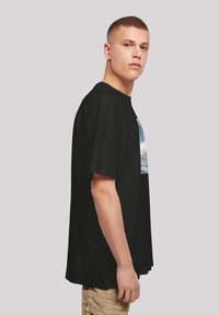 Camiseta negra de manga corta, con un estampado gráfico en tonos azules y grises en la parte frontal. Corte relajado, material de algodón.
