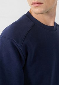 Sudadera azul marino con cuello redondo, hecha de tela suave; presenta mangas raglán y un detalle de costura minimalista.