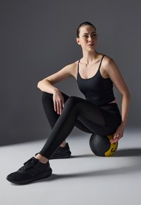 Black athletic outfit consisting of a fitted tank top and leggings, with a textured pattern. Black sneakers, sitting on a black and yellow exercise ball.