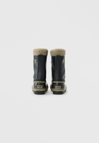 Par de botas de invierno negras con forro de felpa beige, suelas de goma y etiquetas de marca en los talones, mostradas desde atrás sobre un fondo blanco.