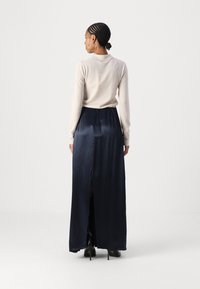 Lichtbeige lange mouwen top gecombineerd met een donkerblauwe satijnen maxi rok met een zijsplit. Zwarte hoge hakken maken de outfit compleet.