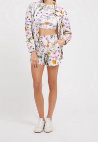 Ensemble crop top et shorts à motif floral dans des couleurs claires, comprenant une veste boutonnée, avec une texture matelassée et deux poches latérales. Baskets blanches.