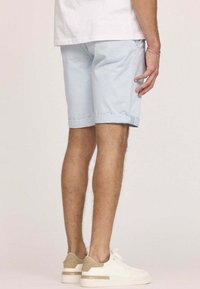 Shorts bleu clair avec des revers, en tissu doux. Baskets blanches avec des accents beige. Poils de jambe visibles et un bracelet simple au poignet.