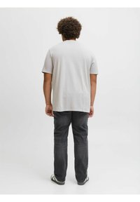 Camiseta de manga corta gris claro, corte holgado, textura suave, combinada con jeans de denim negros, vista trasera, diseño sencillo, con mínimo detalle.