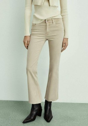 Beige flare jeans van katoen, met een middelhoge taille, vijf zakken en subtiele stikdetails, gecombineerd met zwarte enkellaarsjes.