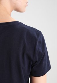 Námorně modré bavlněné tričko s klasickým kulatým výstřihem a krátkými rukávy, které vykazuje hladkou strukturu a minimální švy na límci.