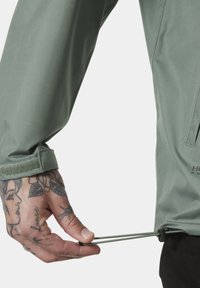 Chaqueta exterior verde con un acabado texturizado. Presenta un cordón ajustable en el dobladillo y un cierre de Velcro en la manga.