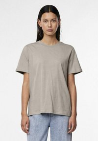 Gara īsām piedurknēm, apļveida kakla t-krekls gaiši pelēkā kokvilnā, ar brīvu piegriezumu un gludu tekstūru. Neformāls dizains kopā ar zilām džinsām.