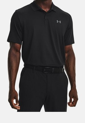 Mężczyzna ubrany w czarną koszulkę polo z krótkim rękawem z logo Under Armour na piersi oraz czarne spodnie z czarnym paskiem.