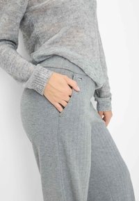 Grijze visgraatbroek met een zijzak en elastische band. Gecombineerd met een lichtgrijze, sprankelende gebreide trui. Zachte textuur en ontspannen pasvorm.