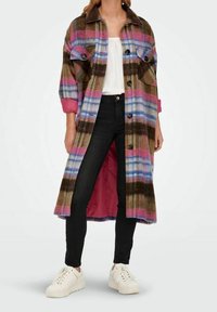 Long plaid coat in brown, pink, blue, and white over white top, black pants, and white sneakers, worn by standing person.